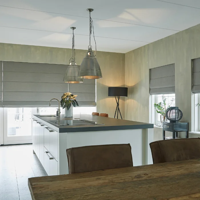 Roman shades on a full wall of windows in a contemporary kitchen with pendant lighting and white cabinetry