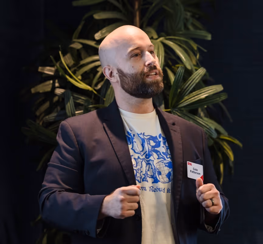 Cole Patterson, founder of heyZensei, is speaking in front of green plants on a dark background.