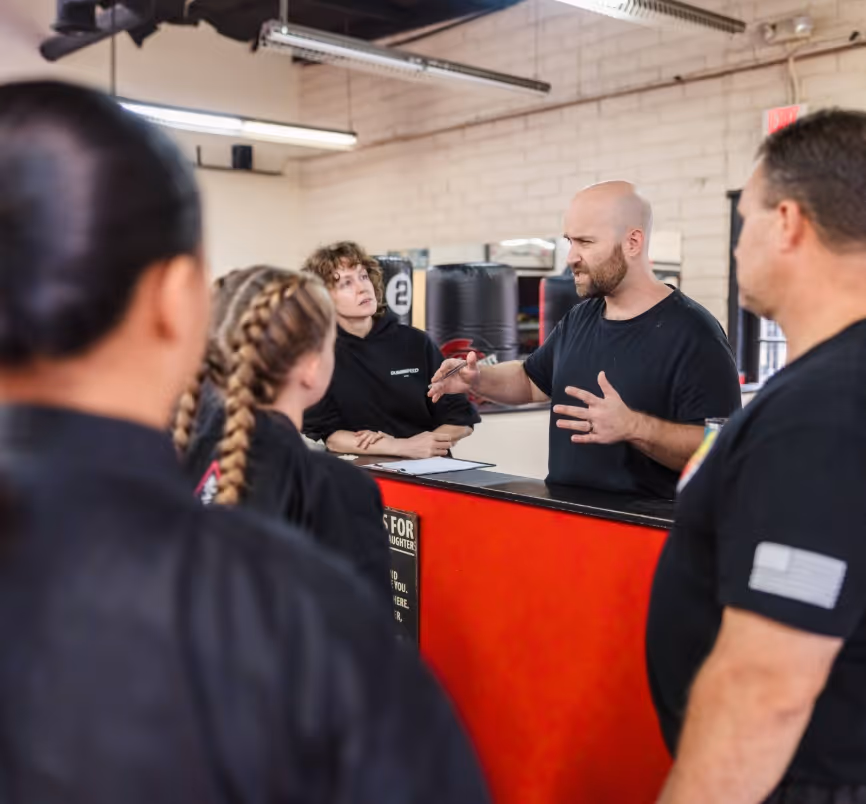 Cole Patterson, founder of heyZenszei, is explaining something to a group in a gym with punching bags.
