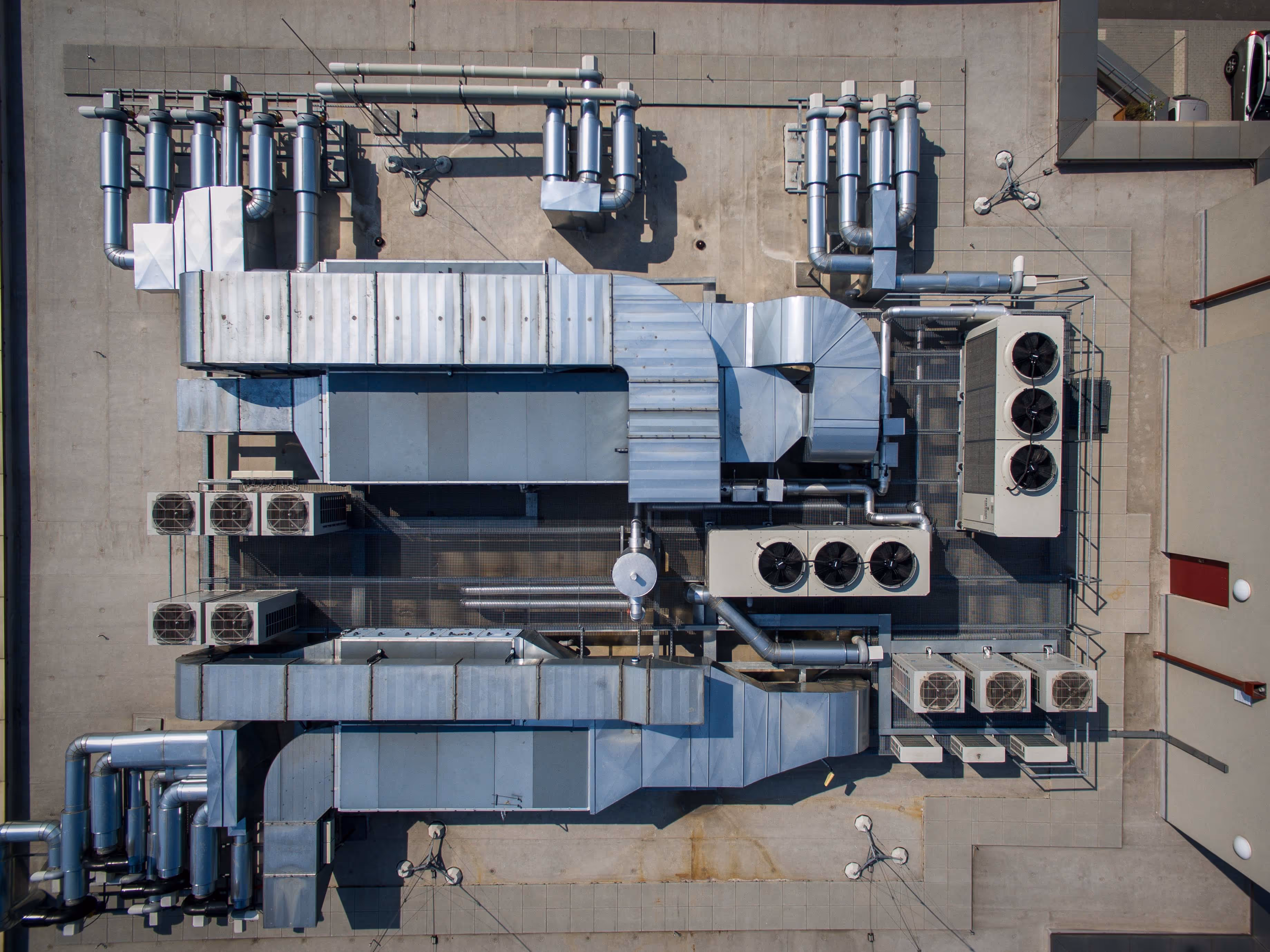 Aerial view of industrial HVAC system with large silver ductwork and multiple cooling units on a flat rooftop.