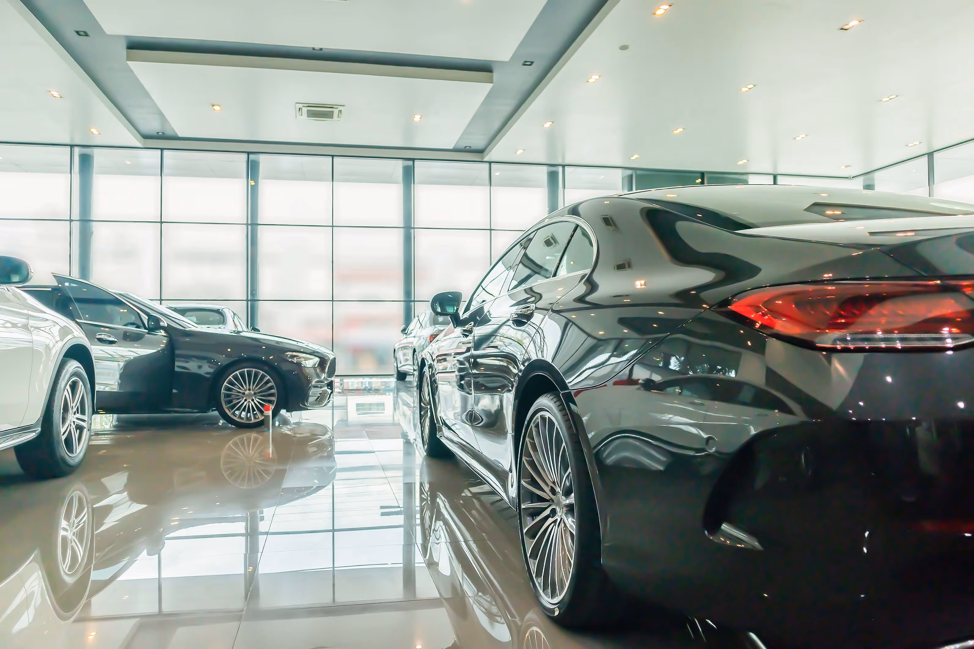 Rows of luxury cars displayed in a bright showroom with glossy tiled floor and large windows.