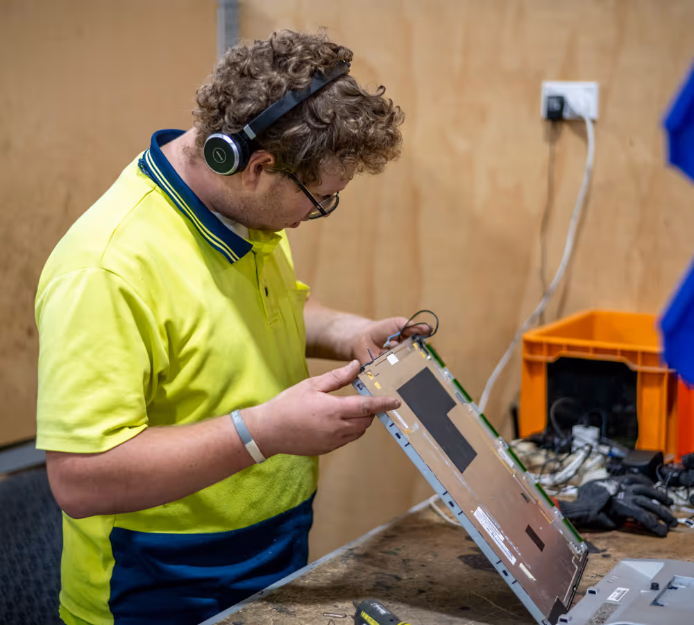 Photo of an e-waste recycling team member taking apart an electrical item