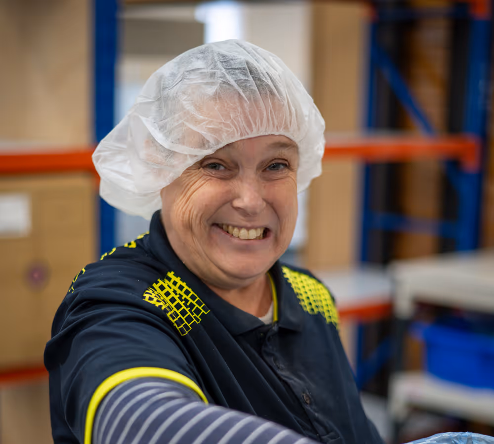 A photo of a Packaging & Manufacturing team member in the food packing department smiling at the camera
