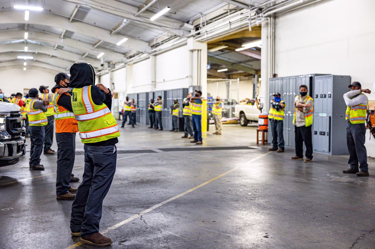 Workers gather inside a warehouse, stretching together in preparation for the day ahead.