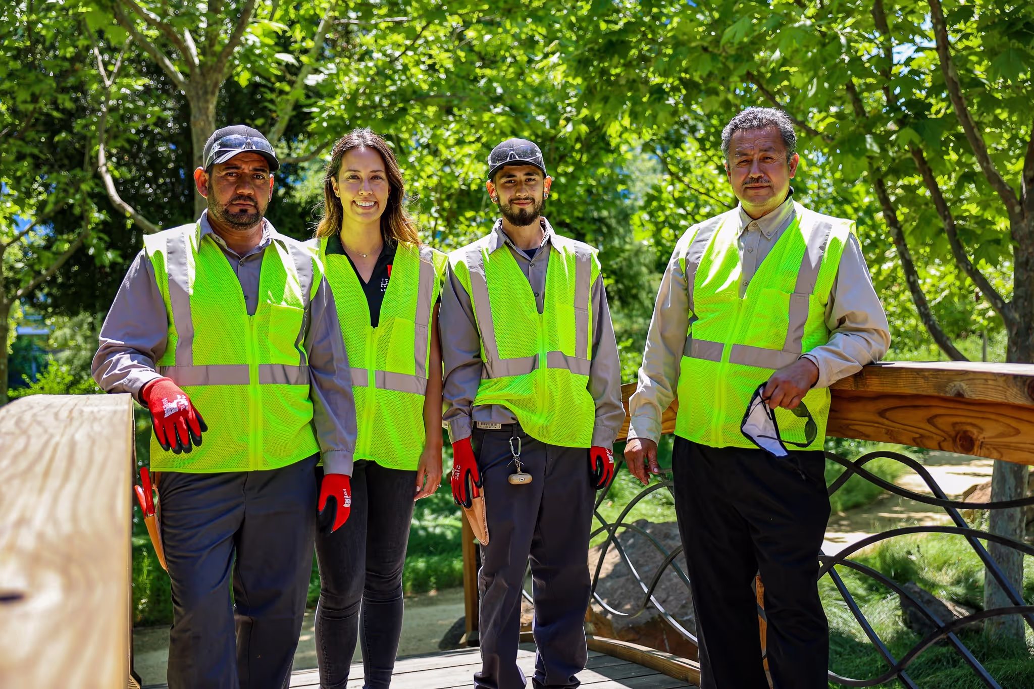 4 workers smiling on a bridge, surrounded by a lush backdrop of trees.