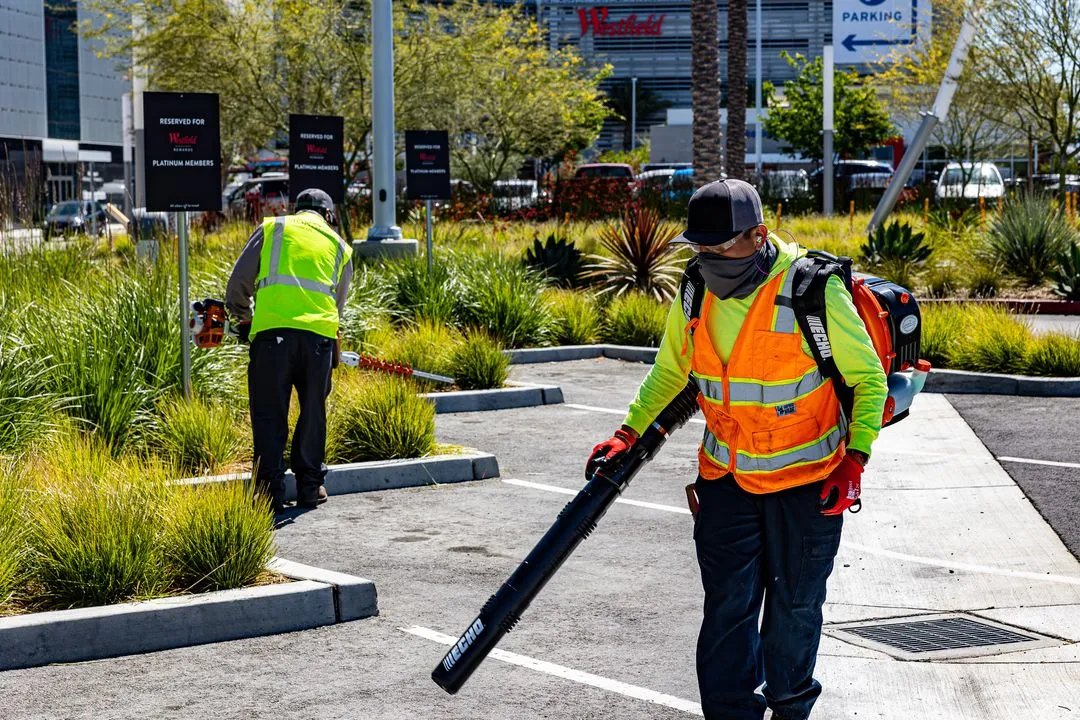 Workers maintaining the landscape of a retail shopping center parking lot. 