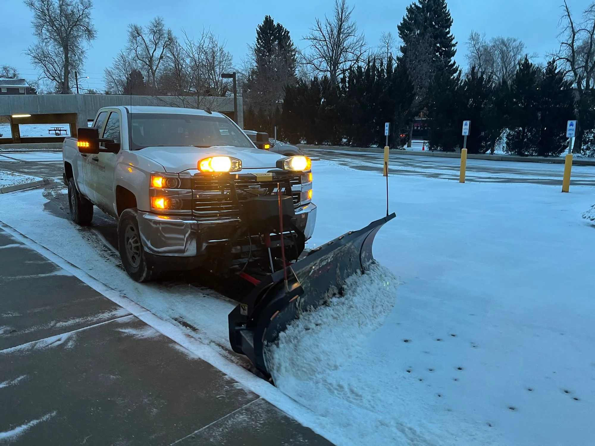 A large truck plows through fresh snow, clearing the wide path of a parking lot.