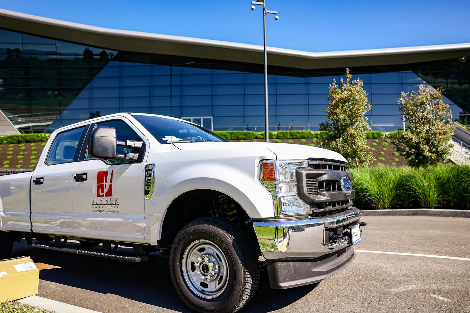 A white truck in front of a commercial building thats outlined with neatly trimmed bushes.