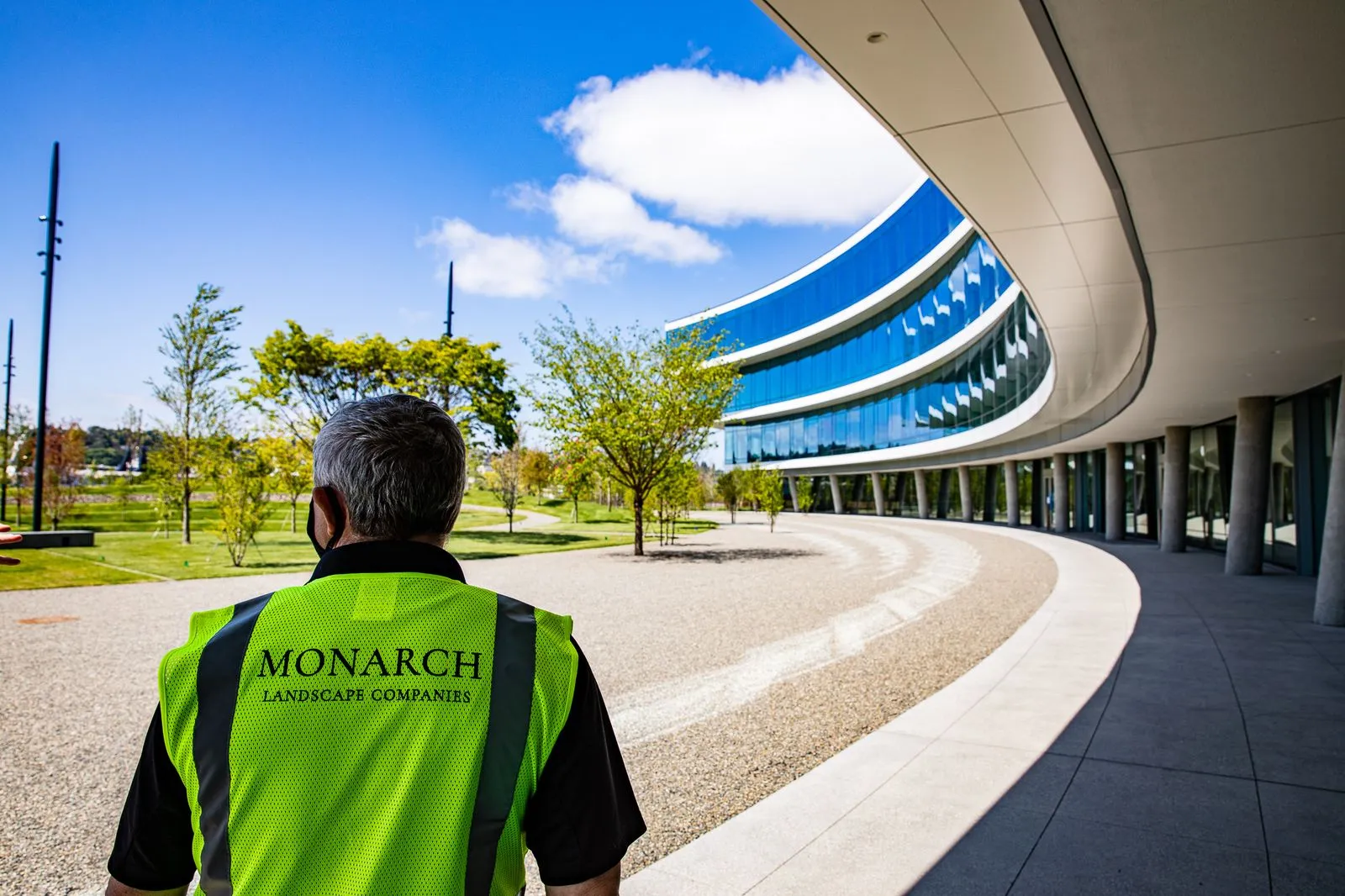 A worker stands admiring the perfectly maincured lawn in front of a commercial building. 