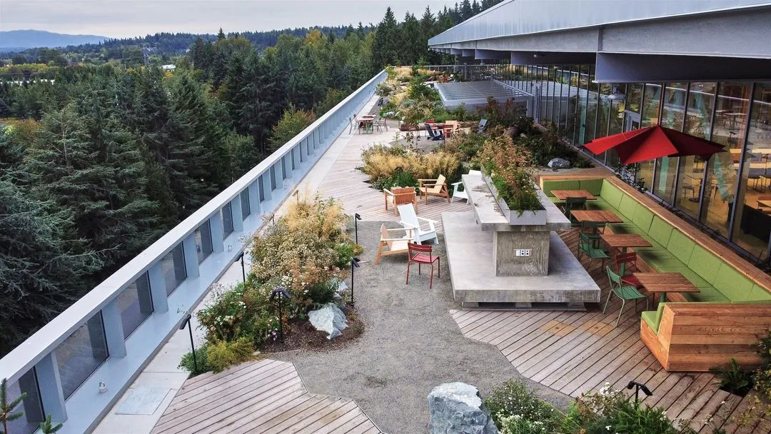 A rooftop balcony stretched across a large commercial building that is covered in well-maintained plants and bushes. 