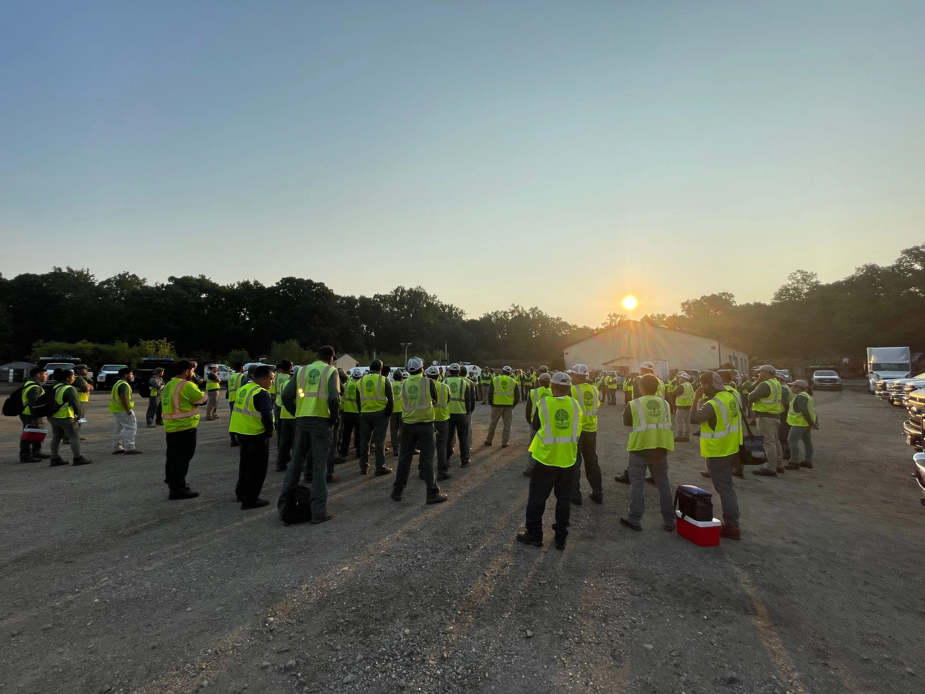 Workers gather around on a dirt field after a day of work.