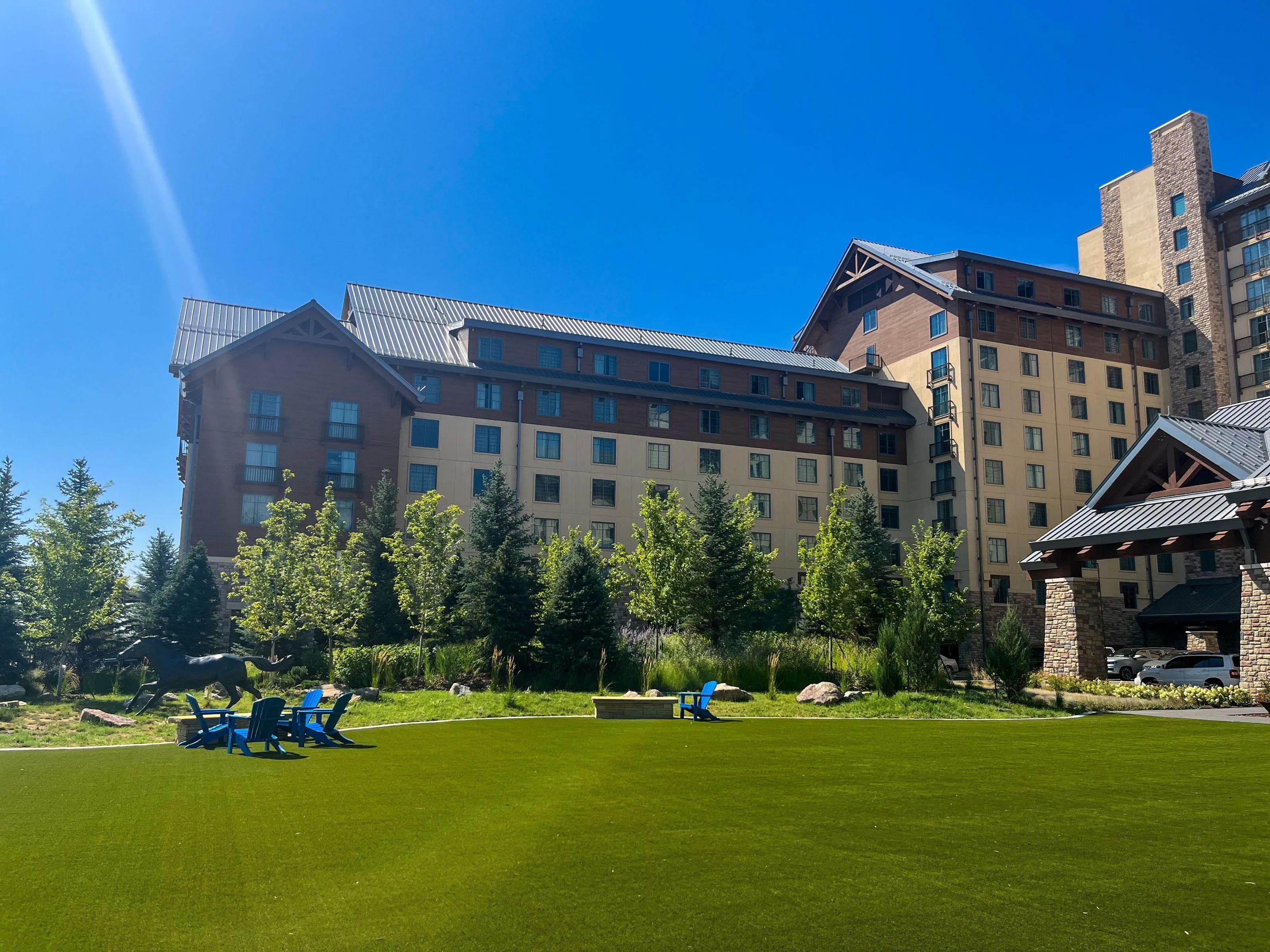 From a distance, Empower Field at Mile High stands proudly on a sunny day, surrounded by a landscape of well-maintained grass and trees.