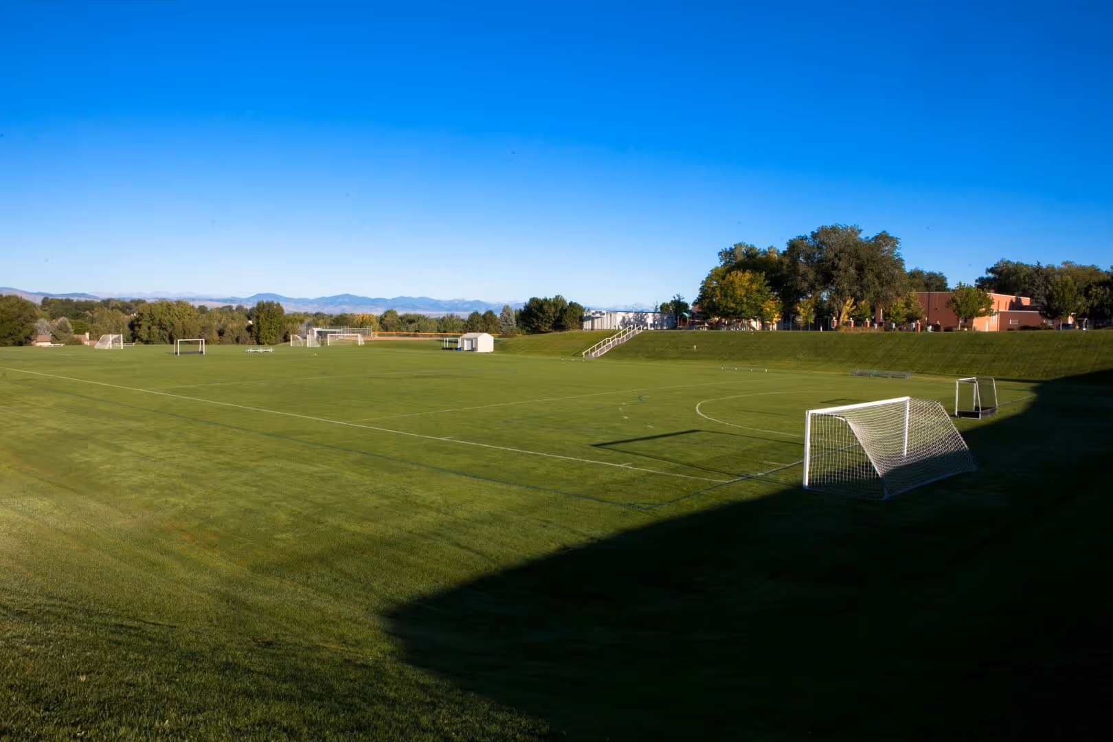 From a distance, Empower Field at Mile High stands proudly on a sunny day, surrounded by a landscape of well-maintained grass and trees.