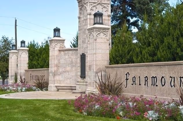 An entrance sign is surrounded by vibrant purple flowers, trimmed grass, and well-maintained trees. 