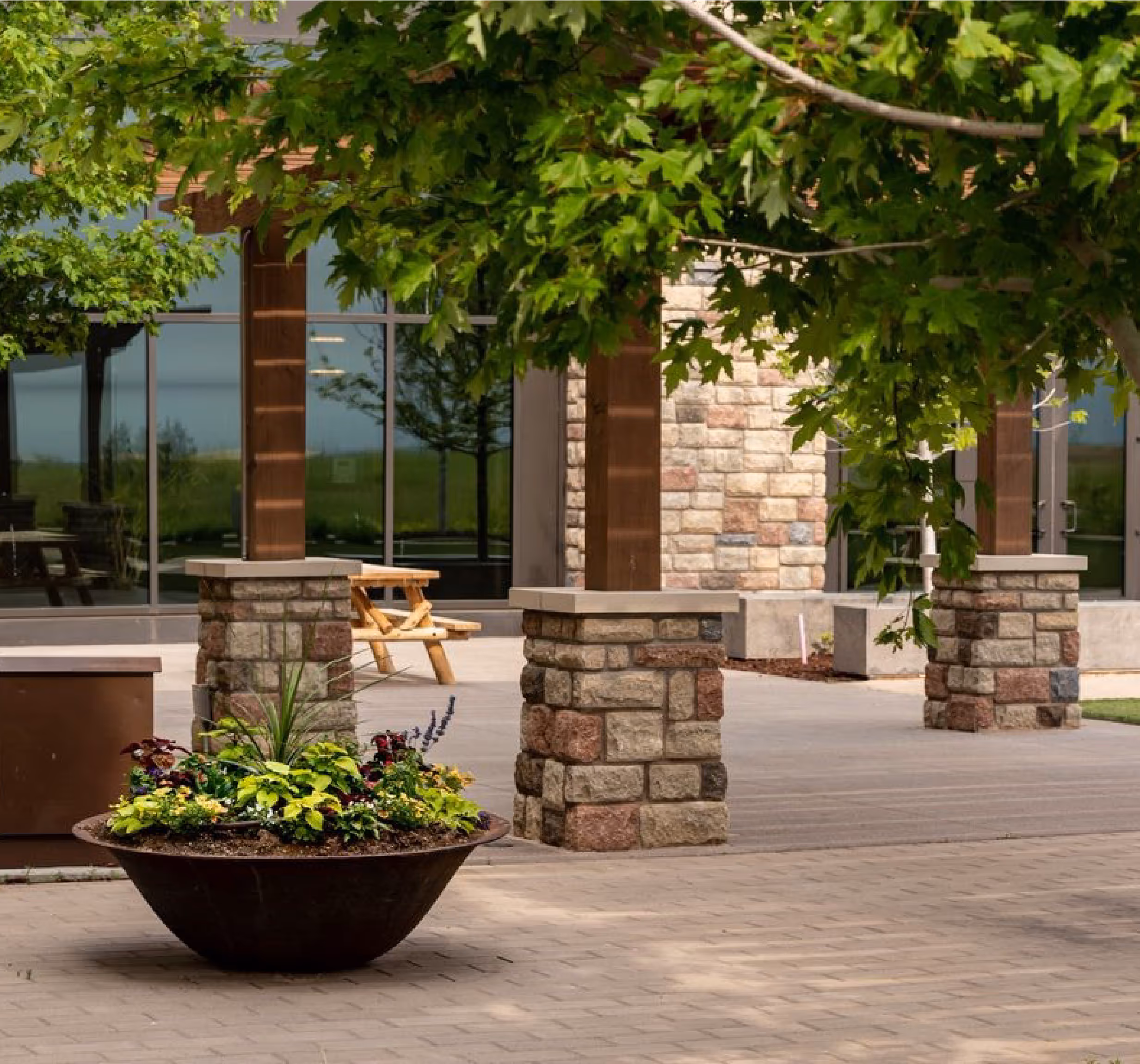 In a commercial seating area, a planter filled with vibrant plants and a towering tree sit at the foreground.