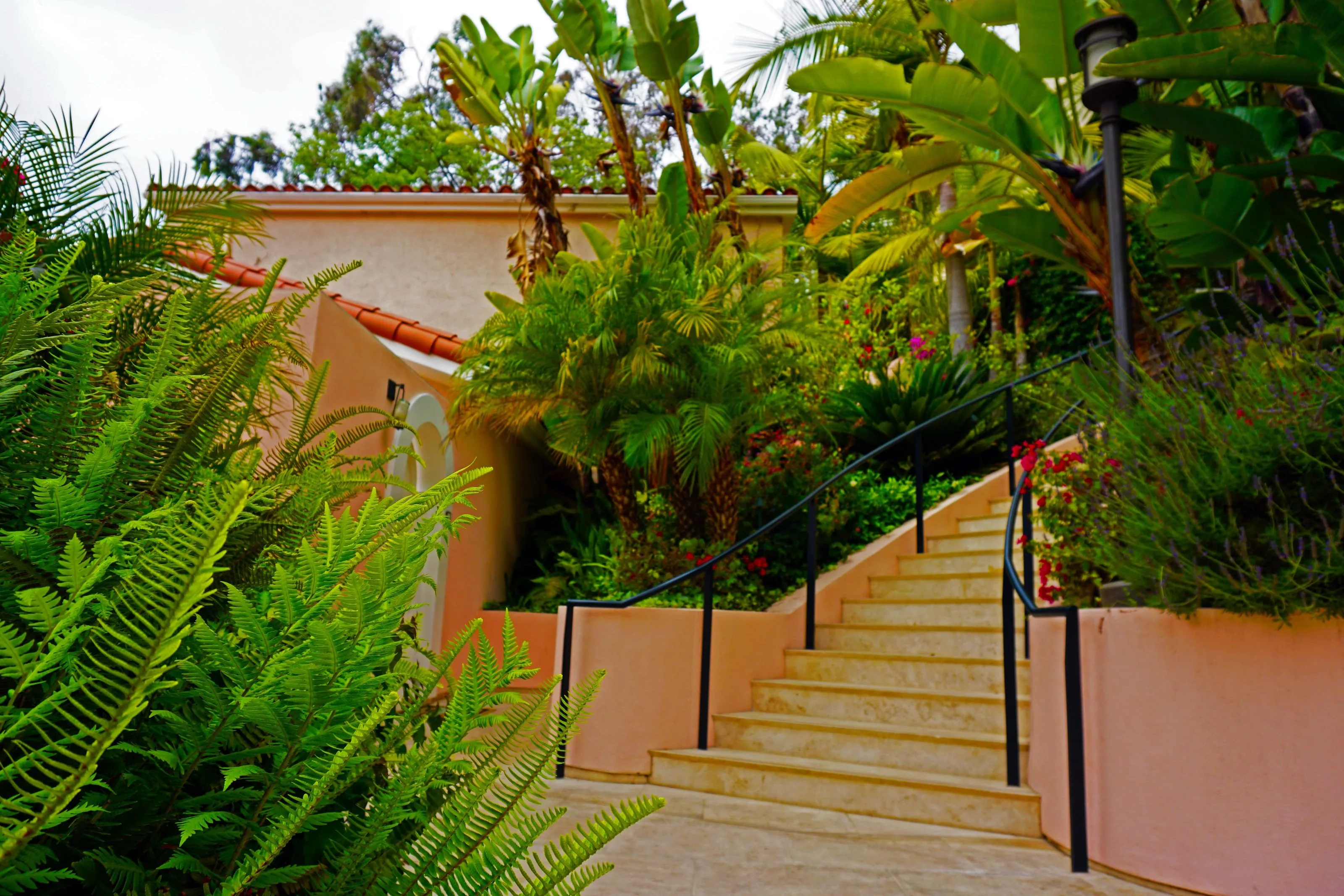Surrounded by rich greenery, a staircase is bordered with blooming flowers and well-maintained palm trees.