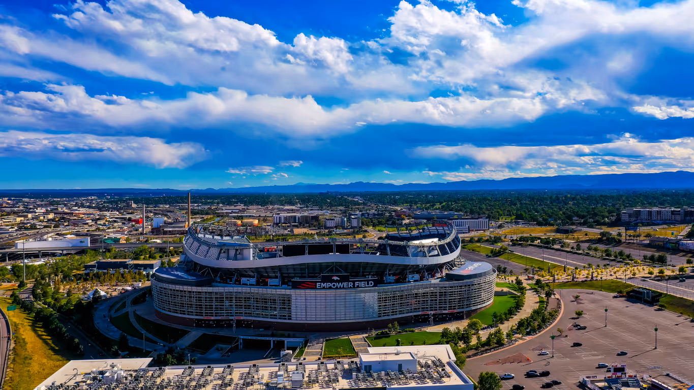 From a distance, Empower Field at Mile High stands proudly on a sunny day, surrounded by a landscape of well-maintained grass and trees.