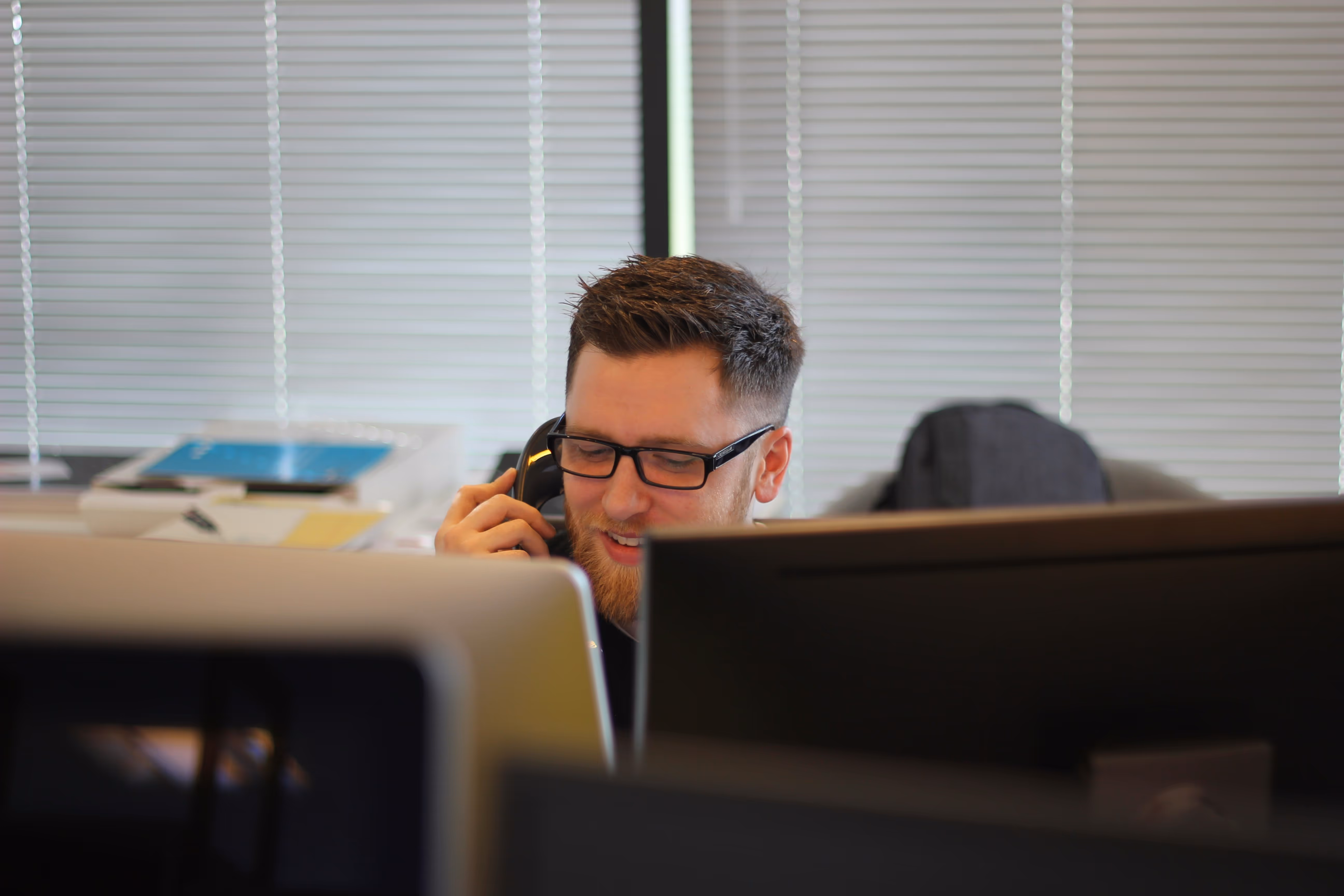 a man at a computer with two monitors talking on the phone