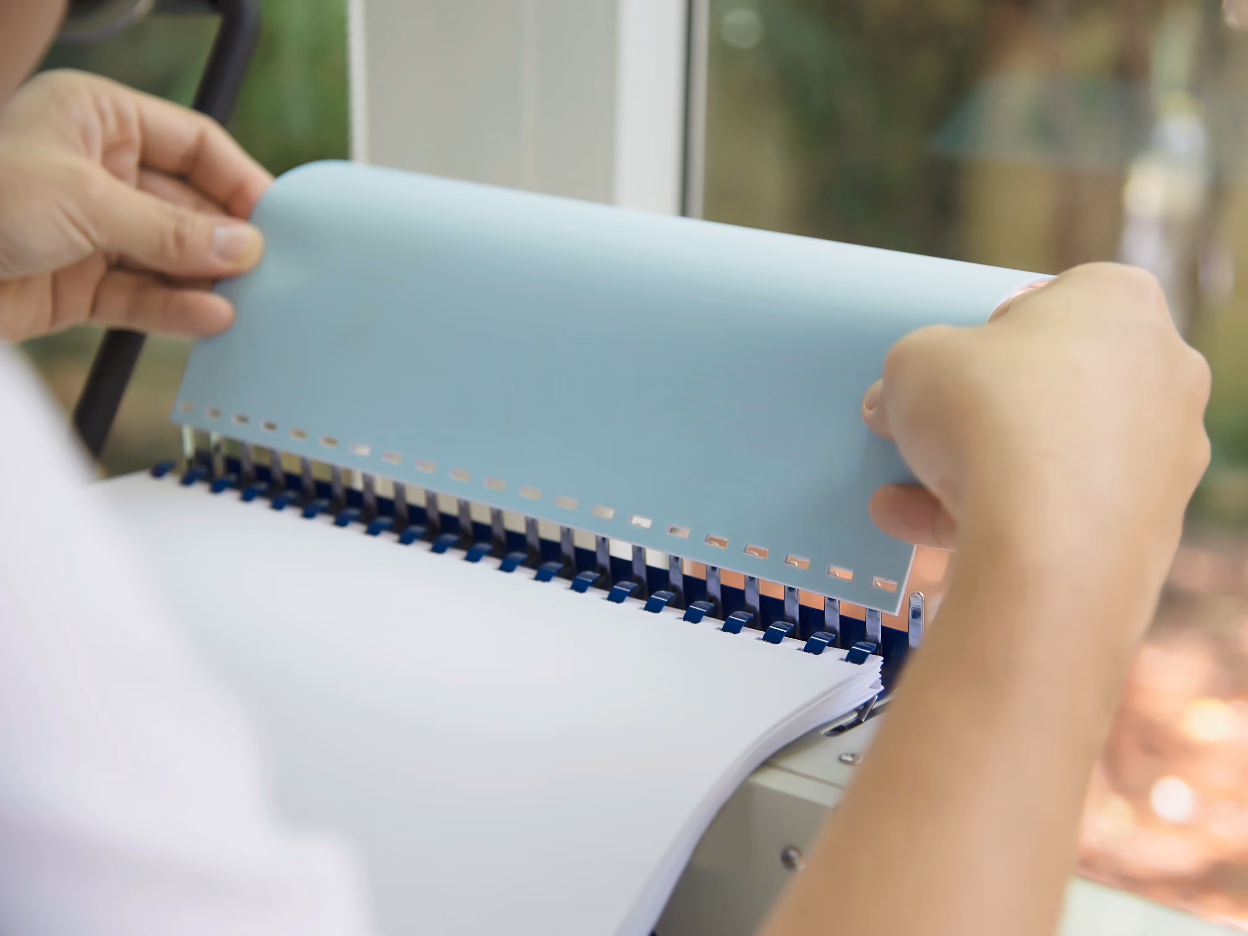 person adding a cover to a comb bound book