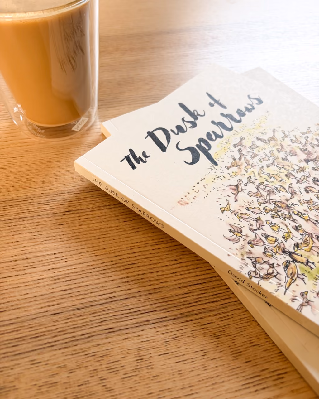 stack of books called dusk of sparrows on a coffee table, next to a coffee mug
