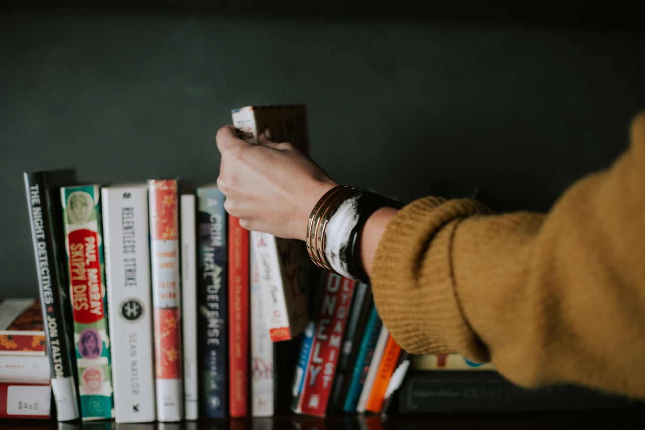person picking up a book from a bookshelf photo by Christin Hume on Unsplash