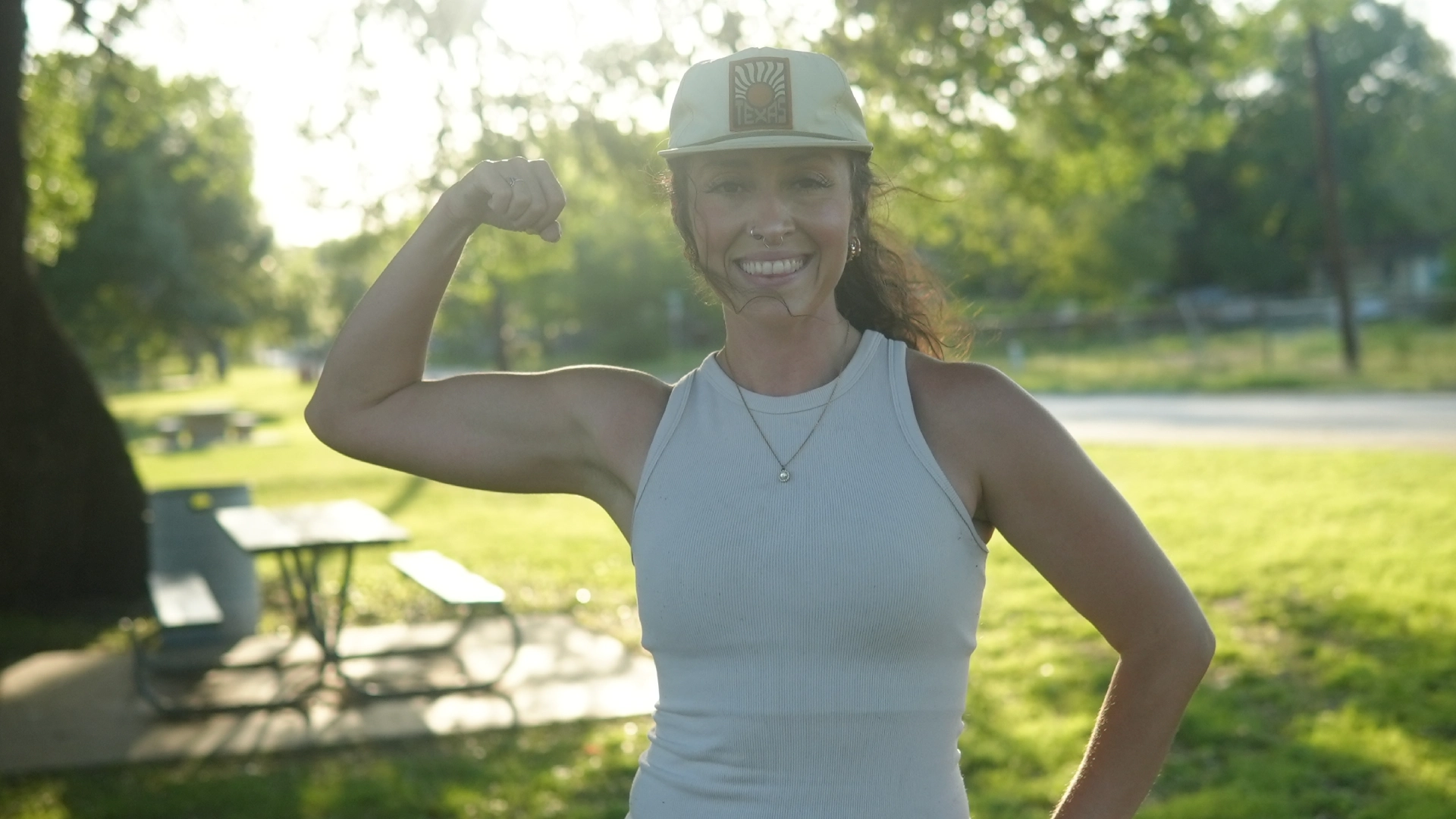 A woman in a baseball cap flexes her muscles at On The Block Fitness in Lockhart, TX, showcasing her strength and confidence.