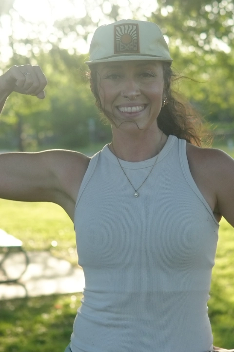 A woman in a baseball cap flexes her muscles at On The Block Fitness in Lockhart, TX, showcasing her strength and confidence.