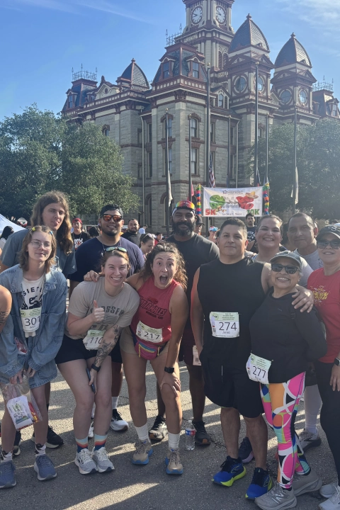 A group of people smiling and posing for a photo after a race at On The Block Fitness in Lockhart, TX.