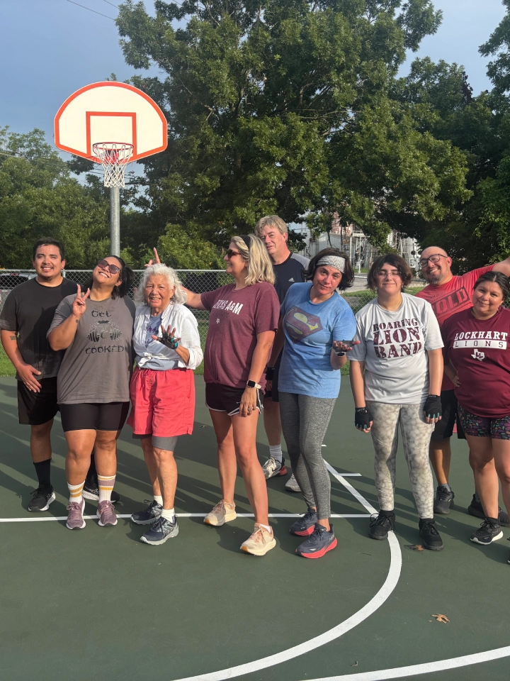 A group of people smiling and posing for a photo on a basketball court at On The Block Fitness in Lockhart, TX.