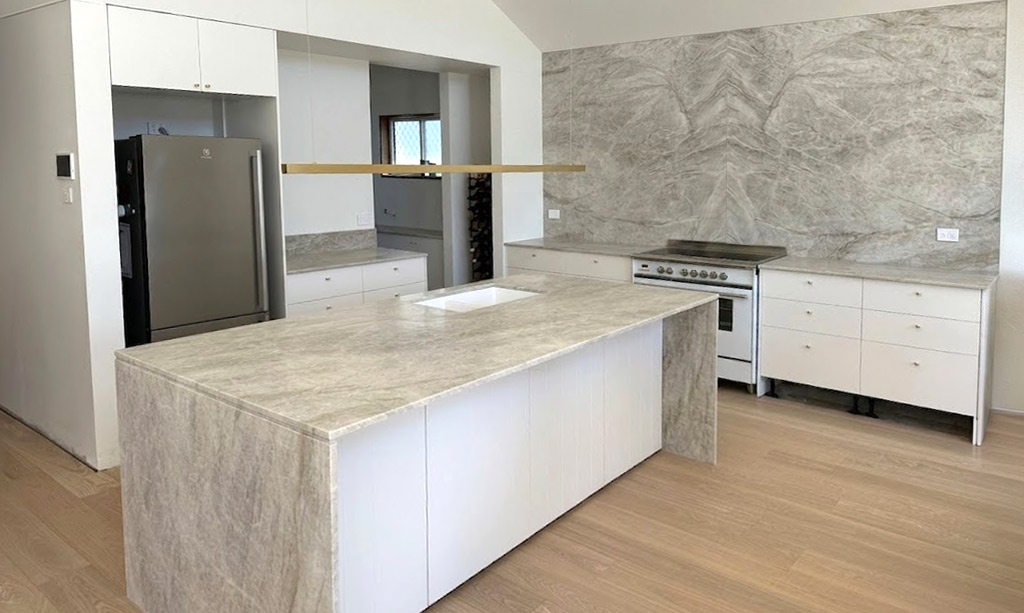 Continuous natural stone benchtop climbing the wall as a full-slab splashback without grout lines.