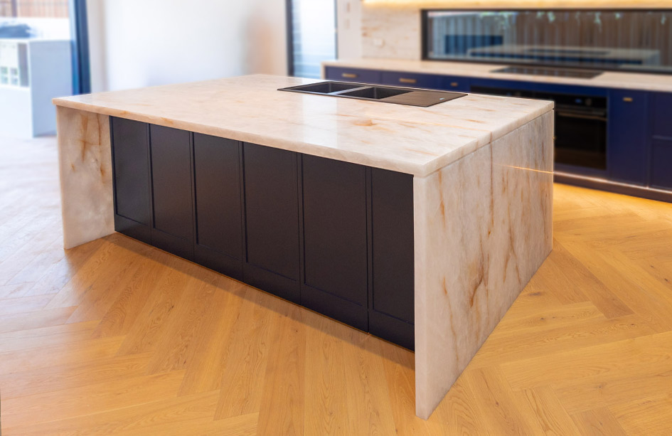 White Cristallo quartzite island benchtop with waterfall edges above navy cabinetry and a herringbone timber floor