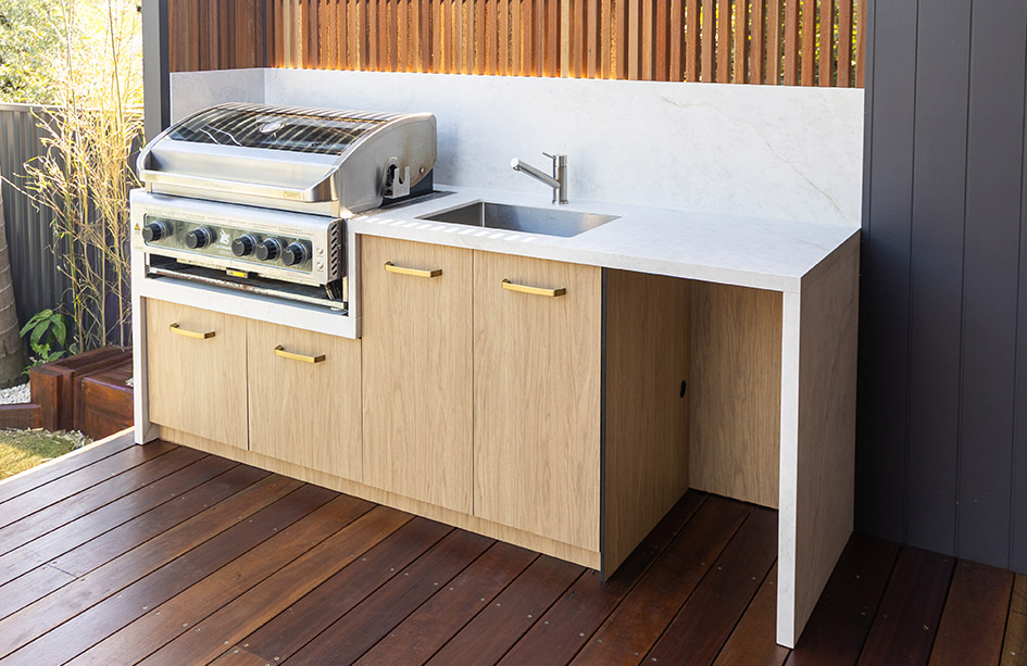 An outdoor alfresco kitchen featuring a heat-proof Everest Sunrise Silk Neolith Porcelain benchtop and splashback. The UV-stable white stone includes a sleek waterfall end, paired perfectly with natural timber decking