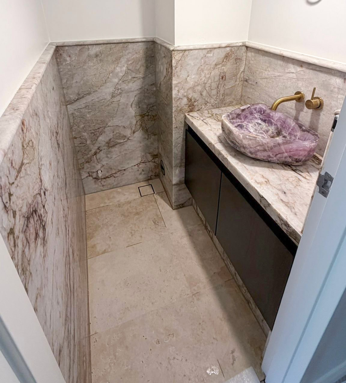 Cristallo Oro quartzite powder room, stone-wrapped walls and vanity, brass wall tap, carved crystal basin