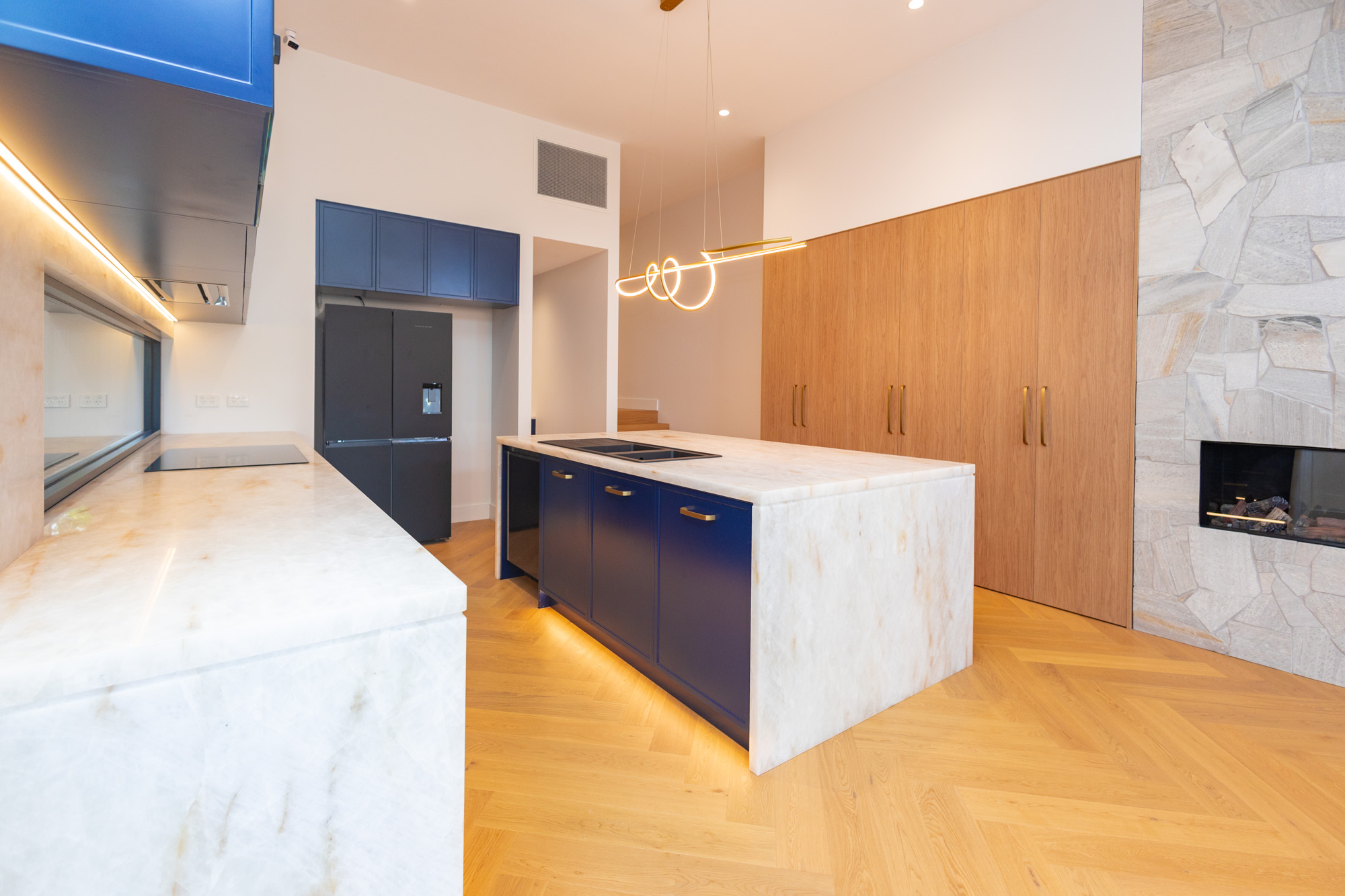 White Cristallo quartzite kitchen with brushed brass handles, navy joinery and warm oak storage, Randwick, Sydney