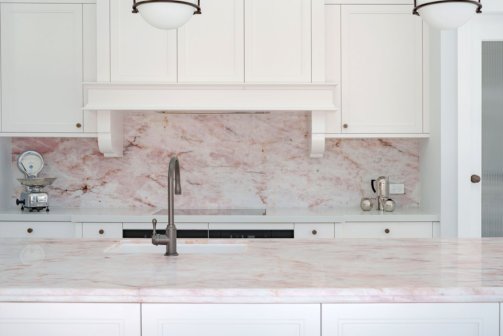 Pink Cristallo Quartzite splashback showing a soft pink crystalline base with gold and dark veining, framed by rangehood corbels