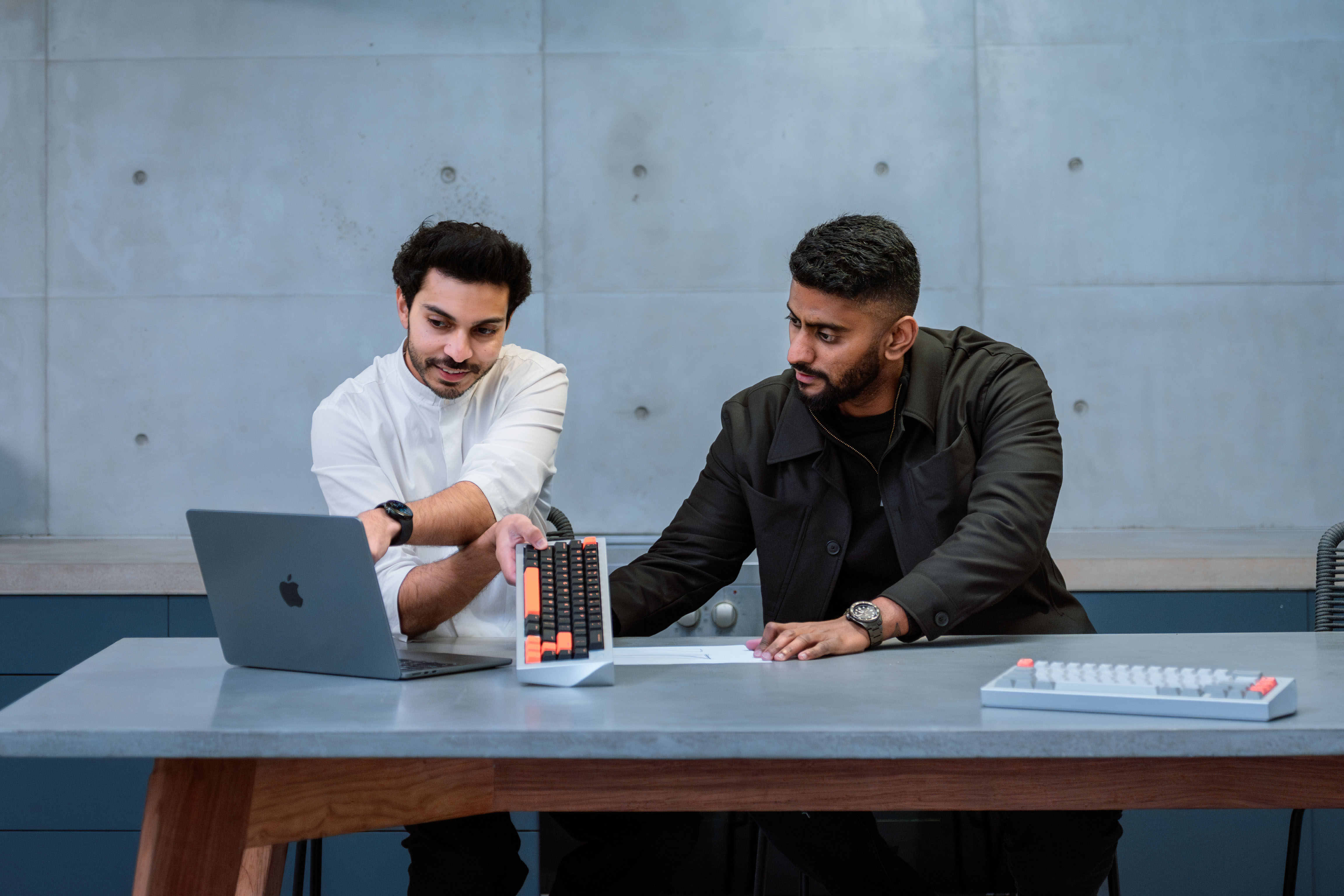 Two men reviewing a mechanical keyboard prototype in a modern workspace, with a laptop and design samples on the table.