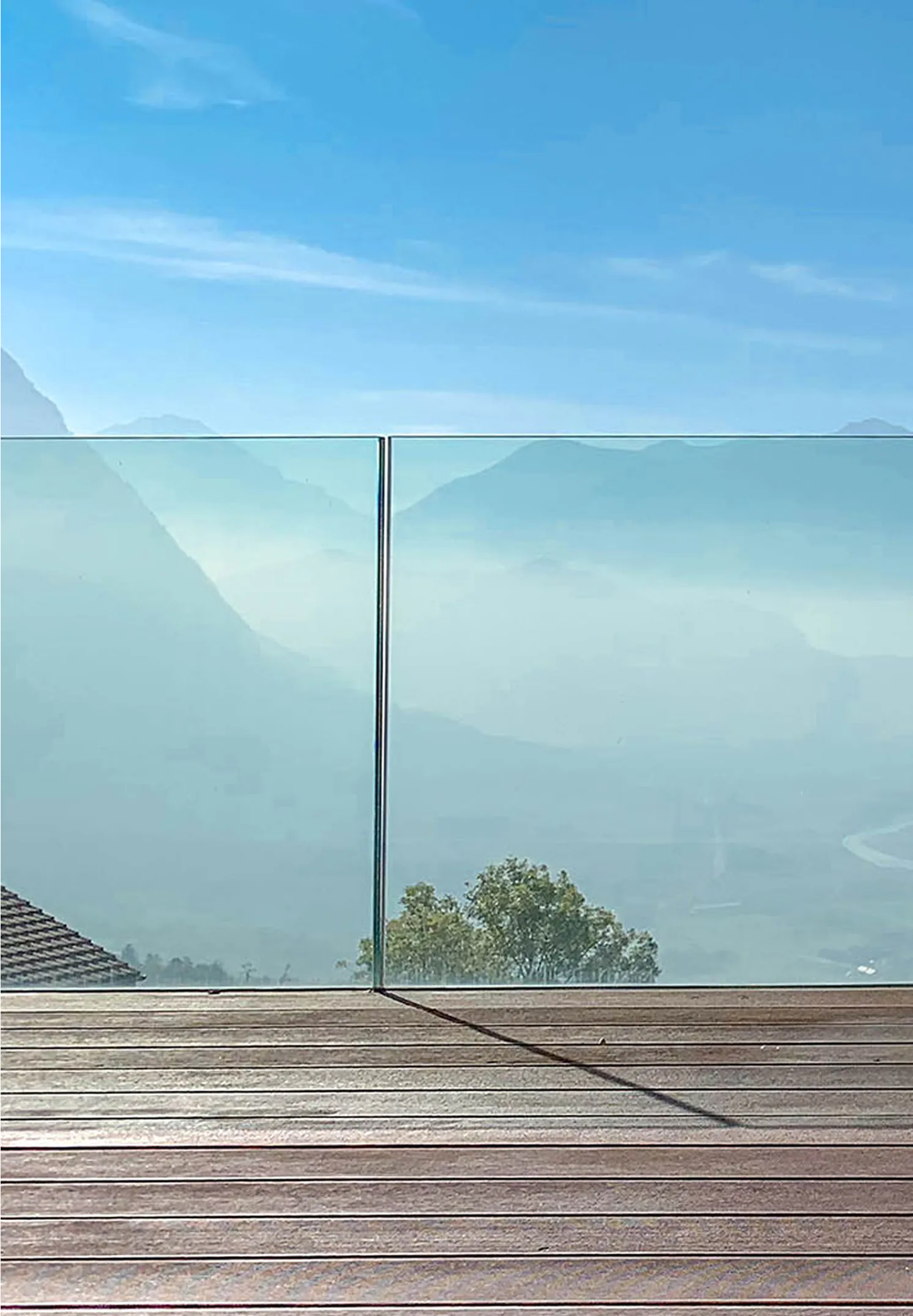 Aussicht von der Terrasse einer Traumimmobilie mit Glasgeländer auf eine majestätische Berglandschaft.