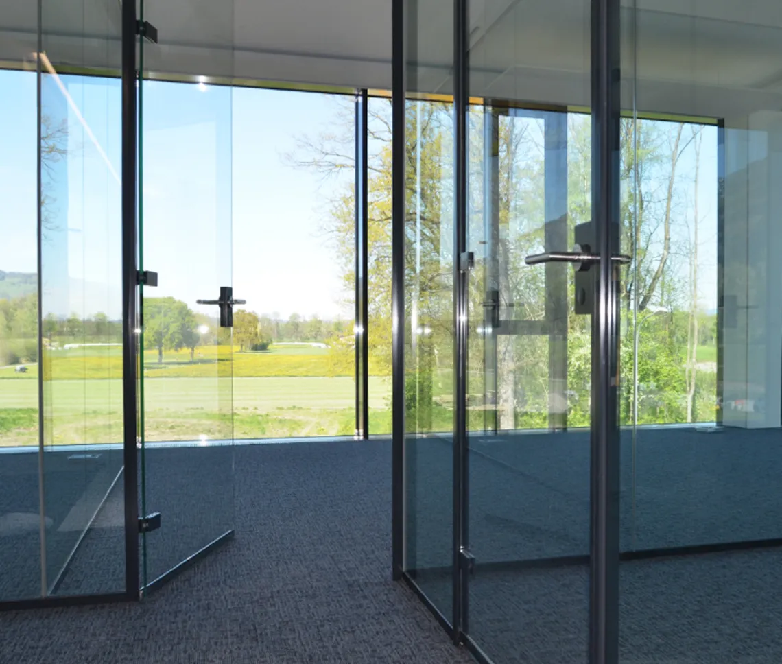Große Glastür in einem Büro mit Glaspartitionen und Blick ins Grüne.