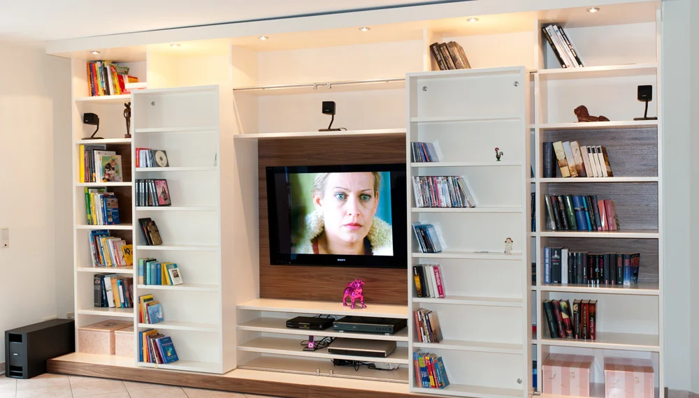Moderne Medienwand mit integriertem Fernseher, offenen Regalen für Bücher und DVDs sowie verstecktem Stauraum in einem Wohnzimmer mit Fliesenboden.