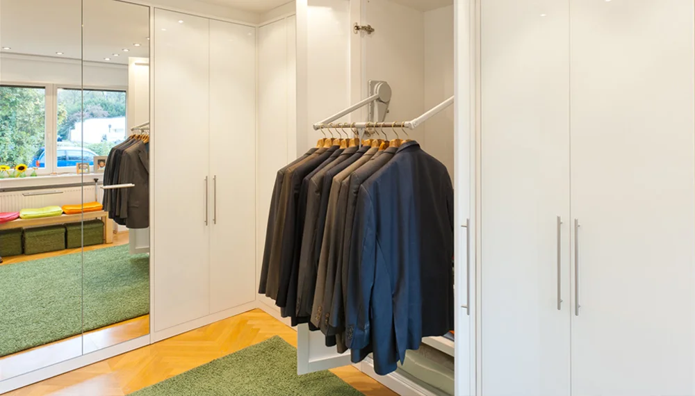 Moderner, weißer Einbauschrank mit ausziehbarer Kleiderstange für Anzüge in einem hellen Ankleidezimmer mit grünem Teppich.