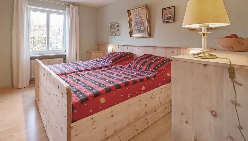 Gemütliches Schlafzimmer mit Möbeln aus hellem Naturholz, zwei Einzelbetten mit roter Bettwäsche in Sonnen- und Mondmotiv, Wandbildern und einer Tischlampe auf einer Kommode.