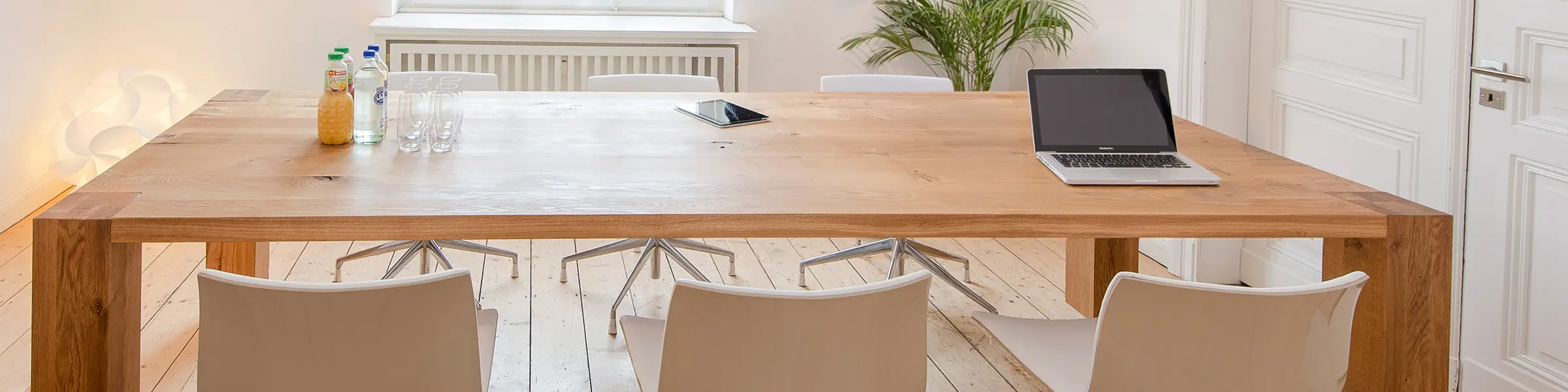 Heller Essbereich mit massivem Holztisch, modernen weißen Drehstühlen und Tischdeko in einem minimalistischen Raum mit Dielenboden.