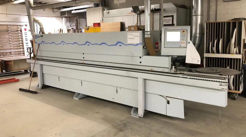 Moderne Kantenanleimmaschine in einer Werkstattumgebung, mit digitalem Bedienfeld und Absaugvorrichtung.