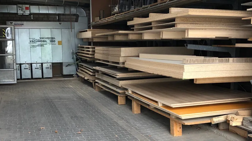 Lagerraum mit gestapelten Holzplatten und Absauganlage im Hintergrund.