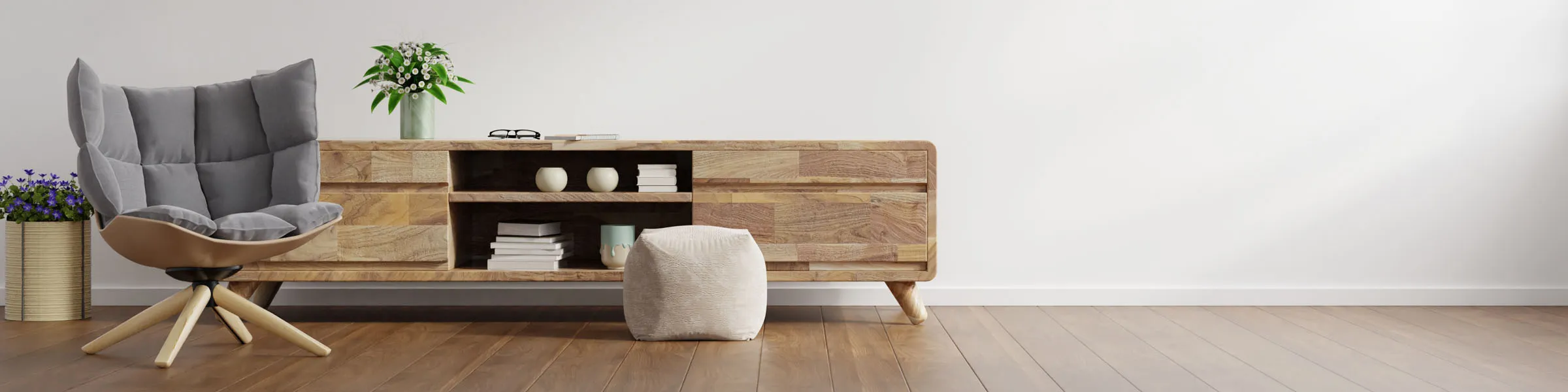 Modernes Wohnzimmer mit gemütlichem grauem Polstersessel, niedrigem Holzsideboard mit offenen Fächern, dekorativen Vasen, Büchern und einem Hocker auf hellem Holzboden vor einer weißen Wand.
