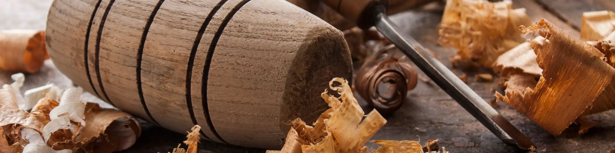 Holzhammer und Stechbeitel auf Werkbank, umgeben von frischen Holzspänen – Symbol für traditionelles Handwerk.