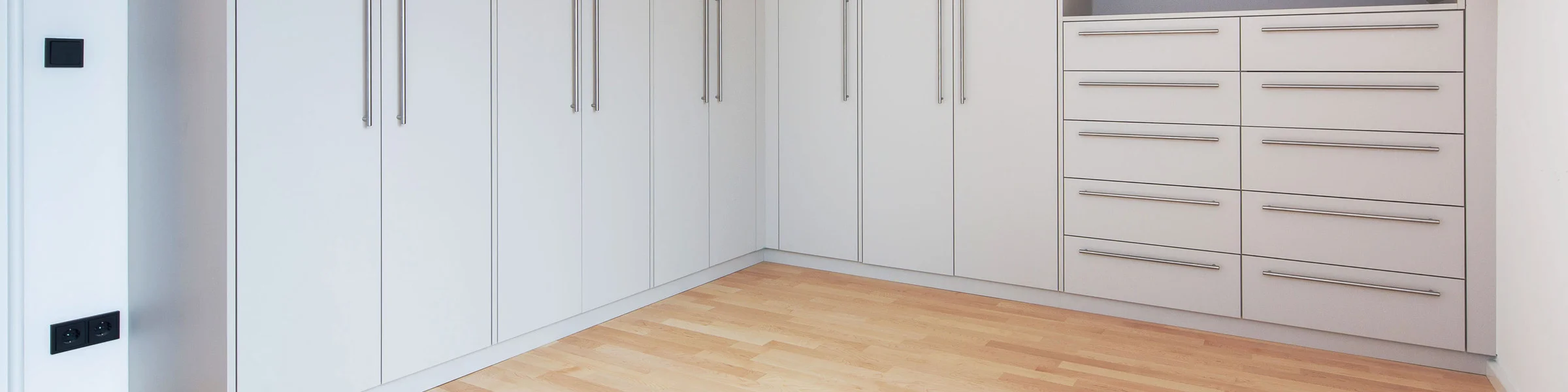 Maßgefertigter Einbauschrank in heller Optik mit Schranktüren, Schubladen und offenen Regalfächern unter einer Dachschräge.