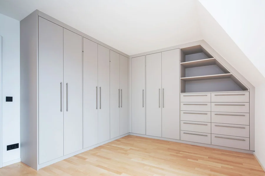 Maßgefertigter Einbauschrank in heller Optik mit Schranktüren, Schubladen und offenen Regalfächern unter einer Dachschräge.