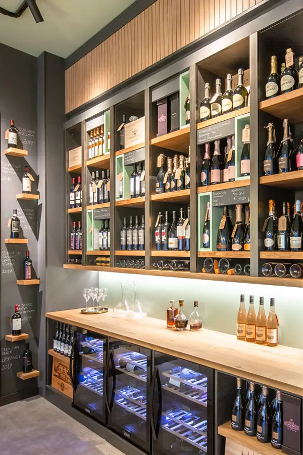 Weinregal mit edlen Champagner- und Weinflaschen im Weinatelier Rochus, darunter stilvolle Weinlagerschränke und eine helle Holztheke mit Gläsern.