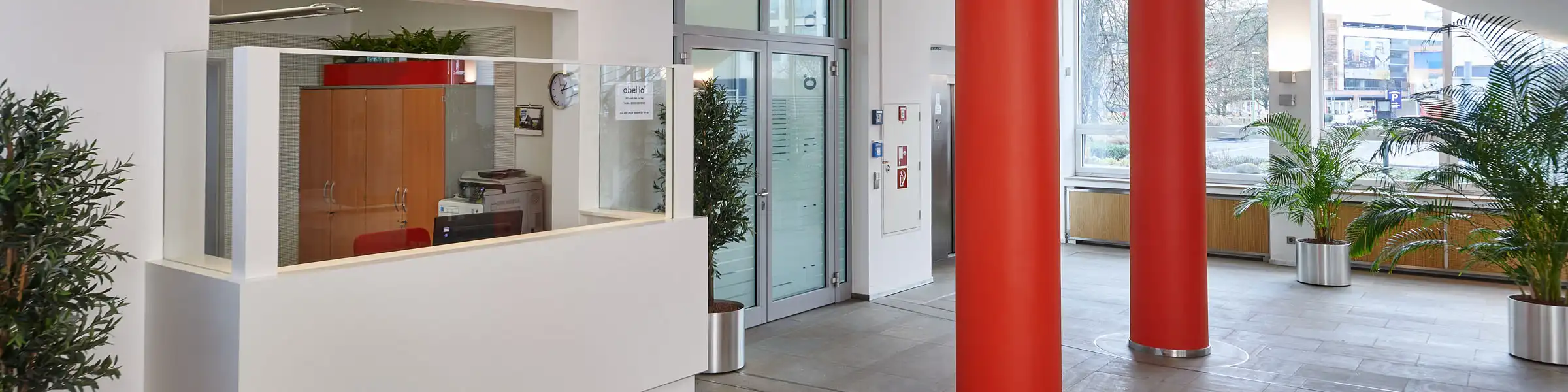 Moderne Empfangshalle im Abellio-Gebäude mit roten Säulen, Glasfront und heller Rezeption im Eingangsbereich.